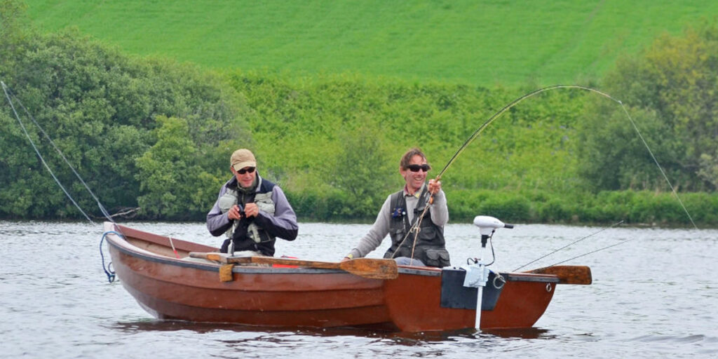 two fly fishermen in boat one fighting a fish