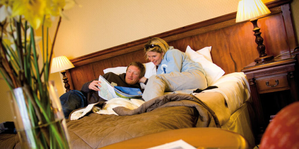 man and woman in hotel bedroom reading guide book