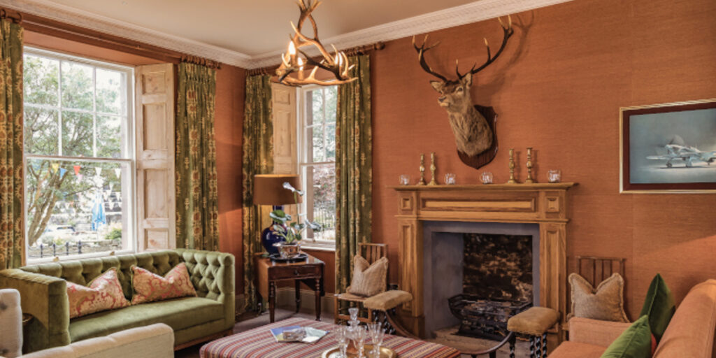 lounge with stags head open fireplace and double aspect windows with green curtains