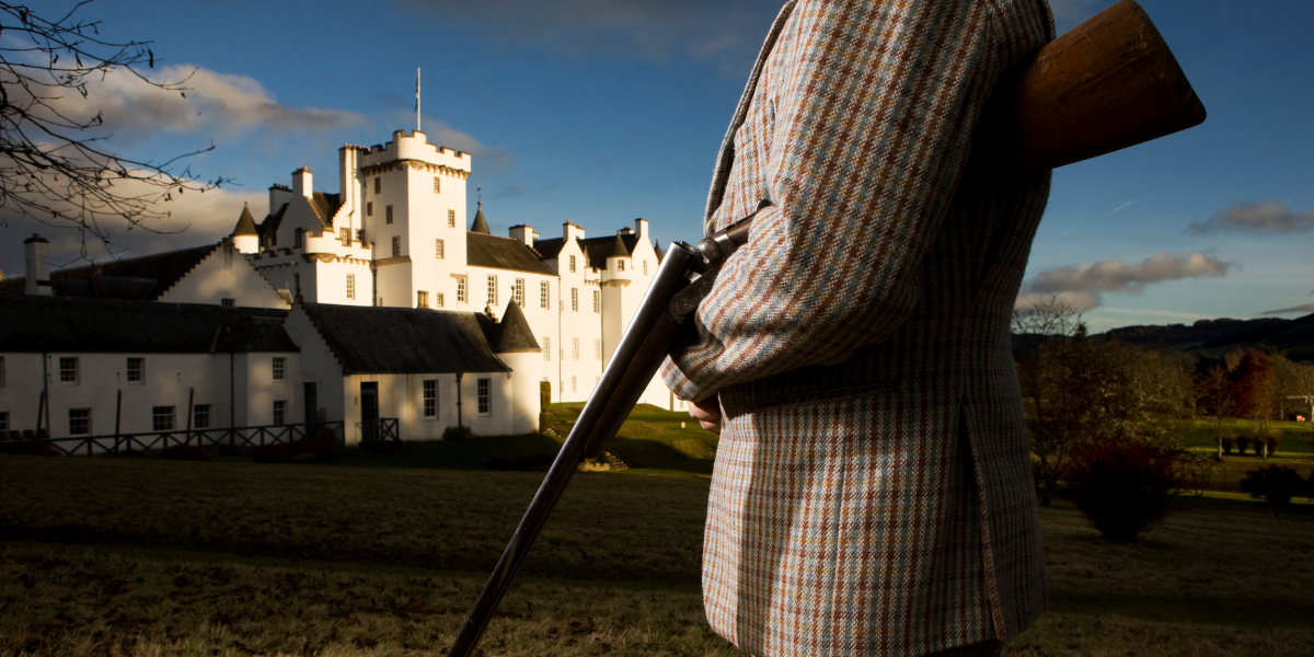 man in tweed with shotgun outside Scottish castle